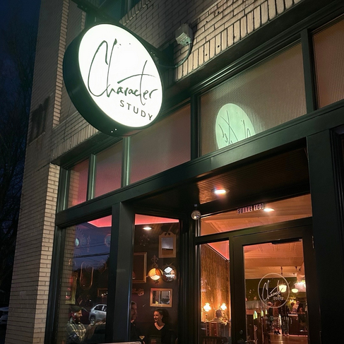 Storefront at night with the lit Character Study signed-circle sign
