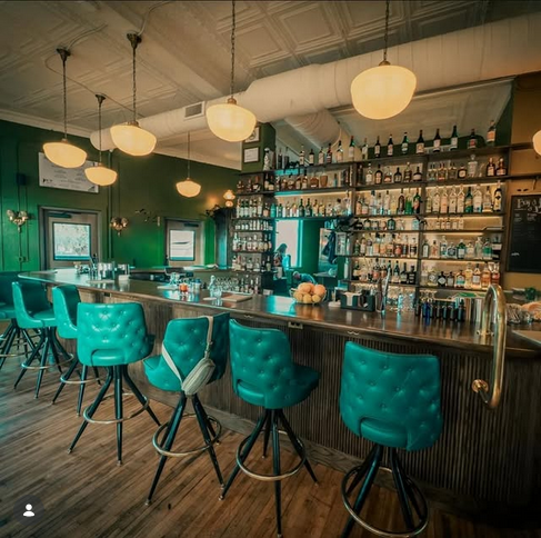 Back-bar with brass pendant lamps and emerald-tufted barstools
