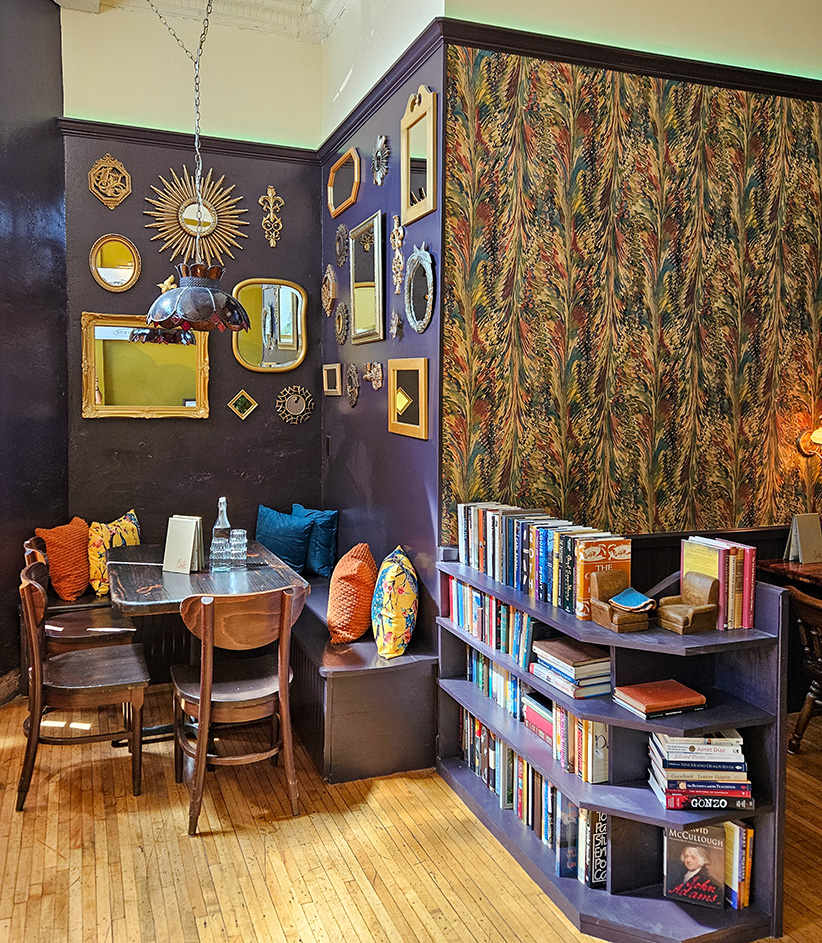 The parlor — banquette seating, gallery-wall mirrors, and bookshelves against marbled wallpaper